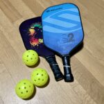 Pickleball paddles and perforated plastic balls laid on wooden surface