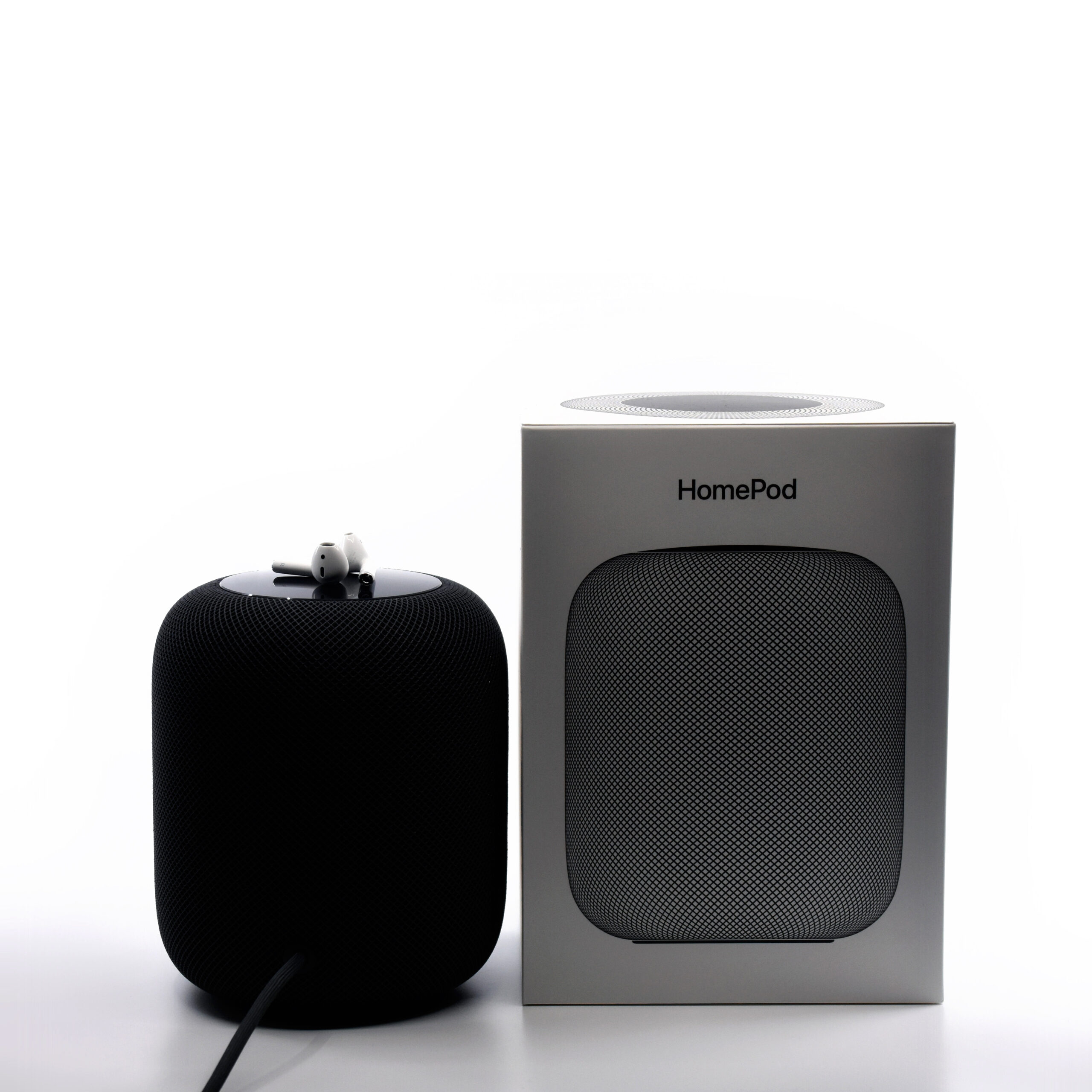 Real photograph of Apple AirPods wireless earbuds beside an Apple HomePod speaker