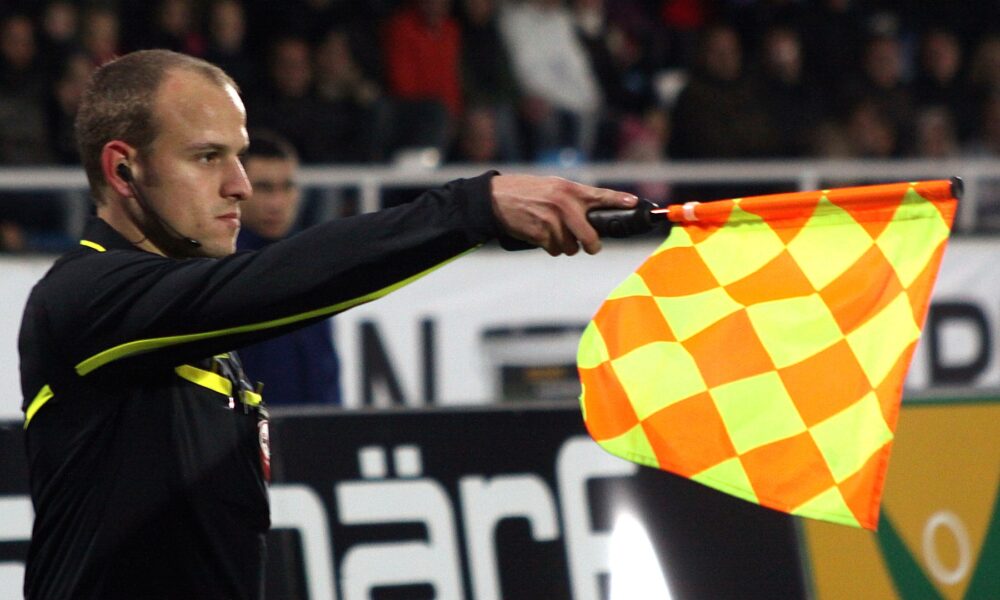 Assistant referee Clemens Schüttengruber raising his flag to indicate an offside decision during a soccer match