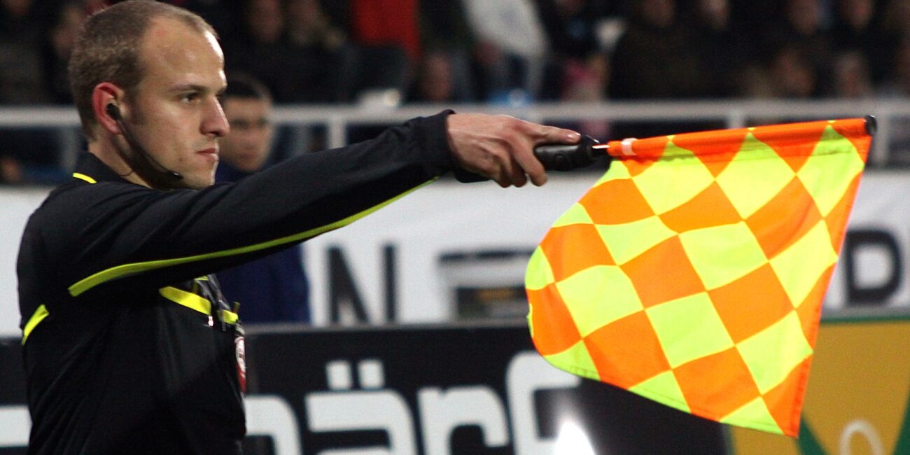 Assistant referee Clemens Schüttengruber raising his flag to indicate an offside decision during a soccer match