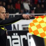 Assistant referee Clemens Schüttengruber raising his flag to indicate an offside decision during a soccer match