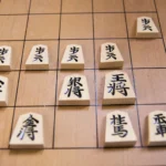 Real wooden shogi pieces, including pawns and generals, arranged on a Japanese chess board