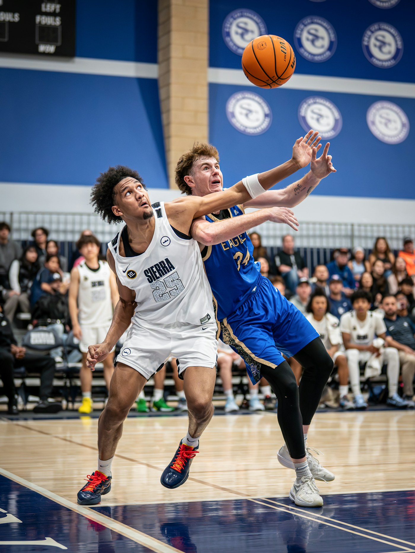 Two basketball players contesting rebound position during a live indoor defensive play