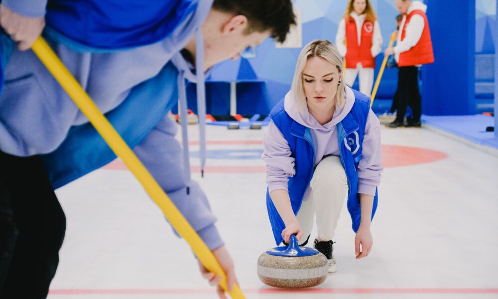 Real curling players sliding and sweeping a curling stone on an indoor ice rink, authentic sport photograph