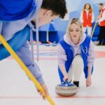 Real curling players sliding and sweeping a curling stone on an indoor ice rink, authentic sport photograph