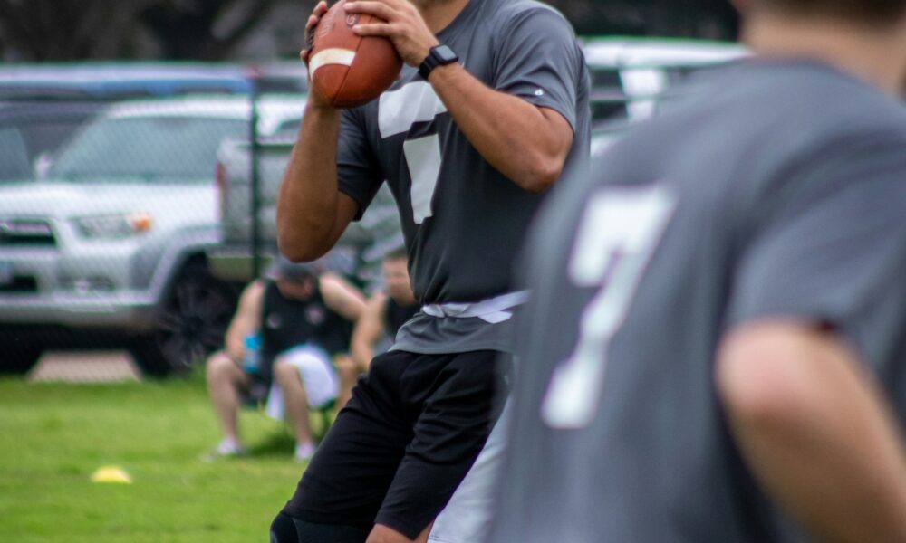A quarterback throwing during a real flag football game, with a yellow flag belt visible on a teammate