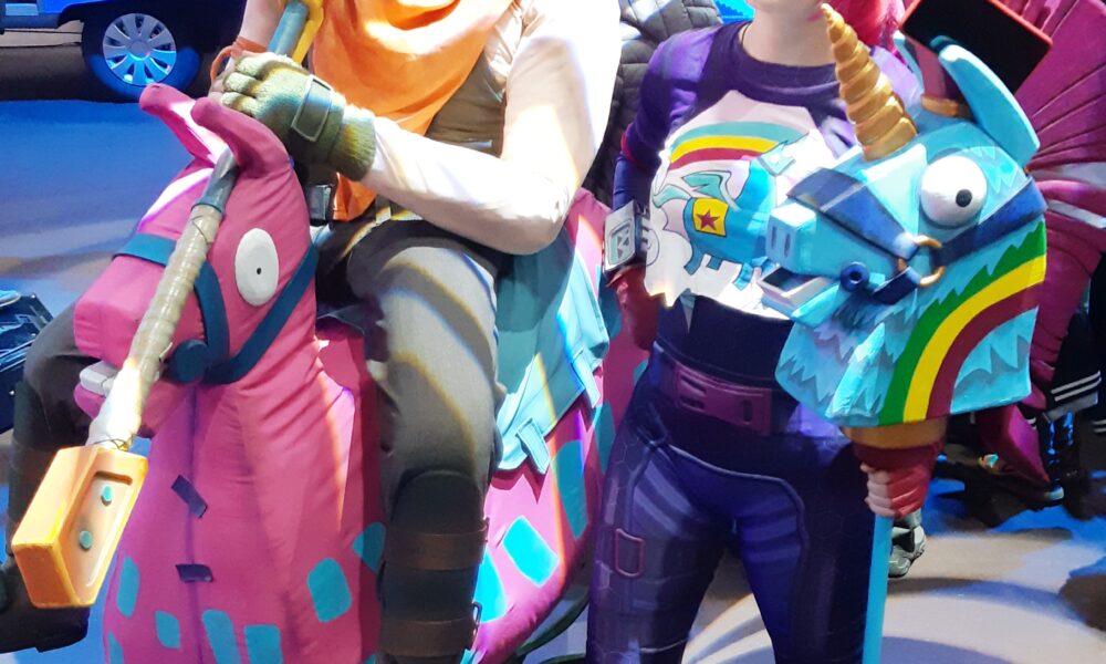 Two Fortnite fans wearing colorful homemade cosplay and llama-themed props at a 2019 gaming convention