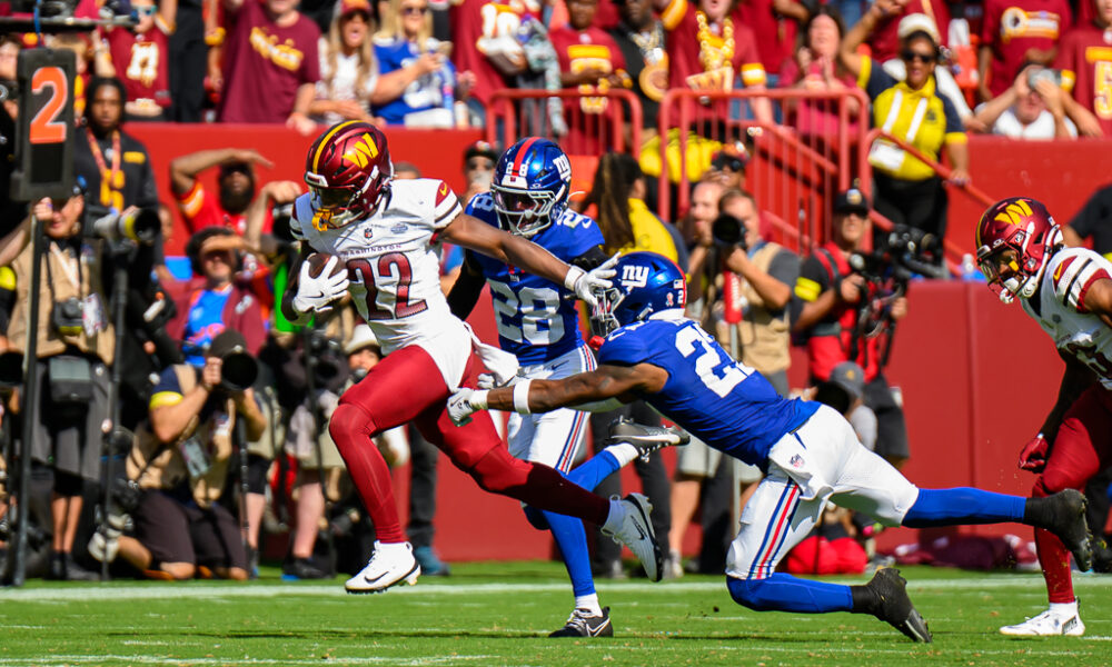 Washington Commanders player carrying the football while two New York Giants defenders pursue during their September 2025 matchup, archival game photo