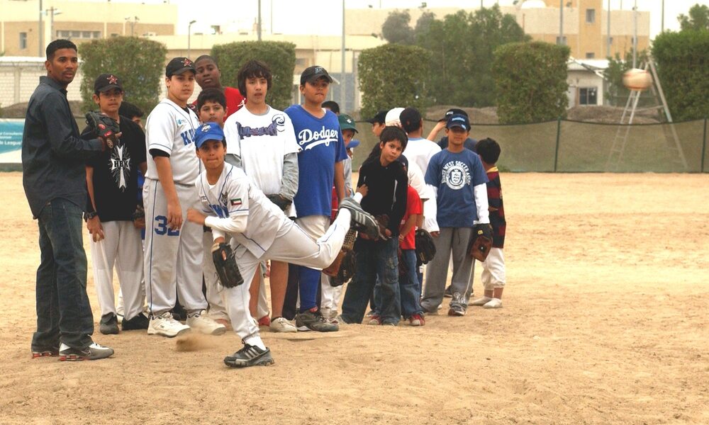 Little League youth baseball pitcher releases a pitch as teammates observe