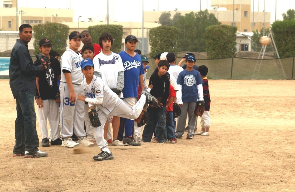 Little League youth baseball pitcher releases a pitch as teammates observe