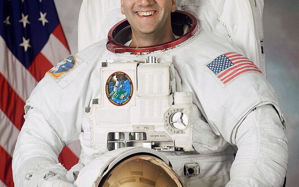 NASA astronaut Michael J. Massimino in a 2001 official portrait wearing a white spacewalking suit