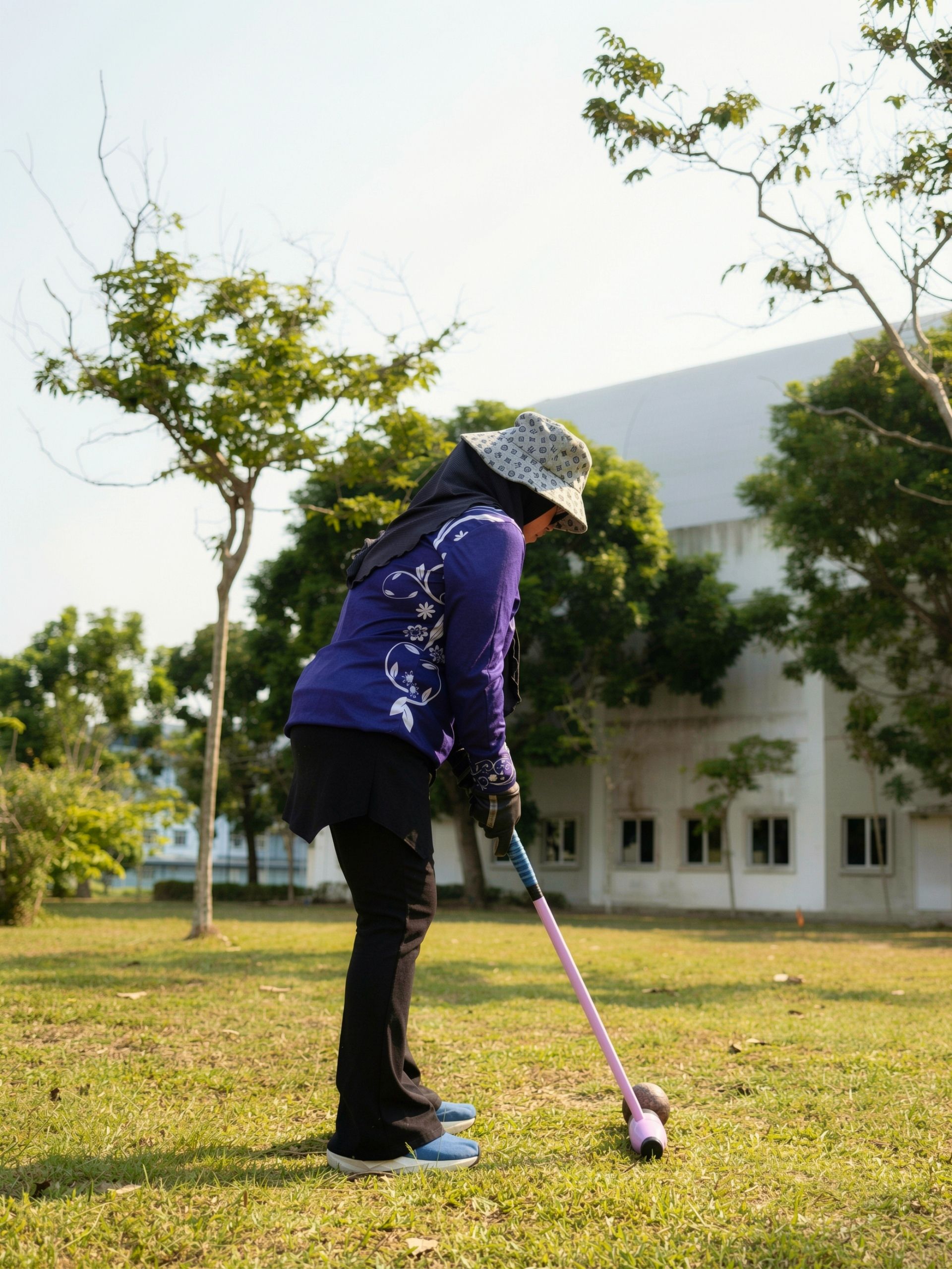 A croquet player lines up a shot with a mallet on the grass