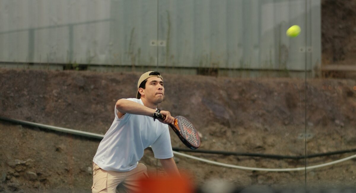 Real padel player hitting a yellow ball on a blue enclosed court in Ensenada, Mexico