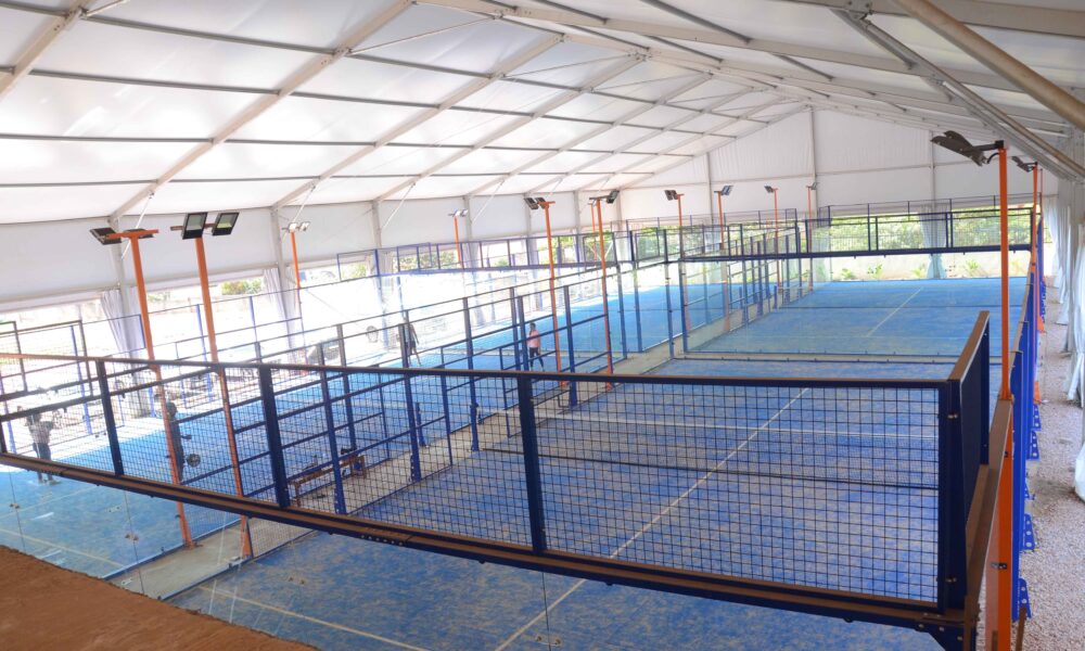 Enclosed padel courts with surrounding glass and mesh walls, unlike the open layout of a pickleball court