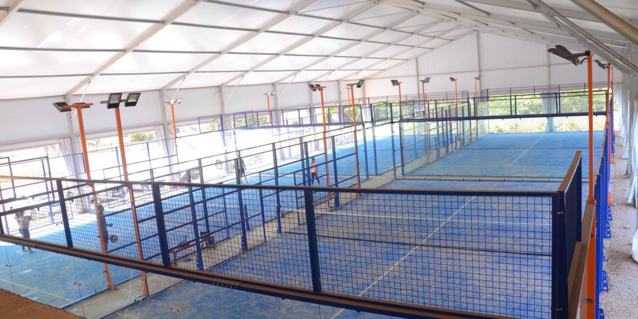 Enclosed padel courts with surrounding glass and mesh walls, unlike the open layout of a pickleball court