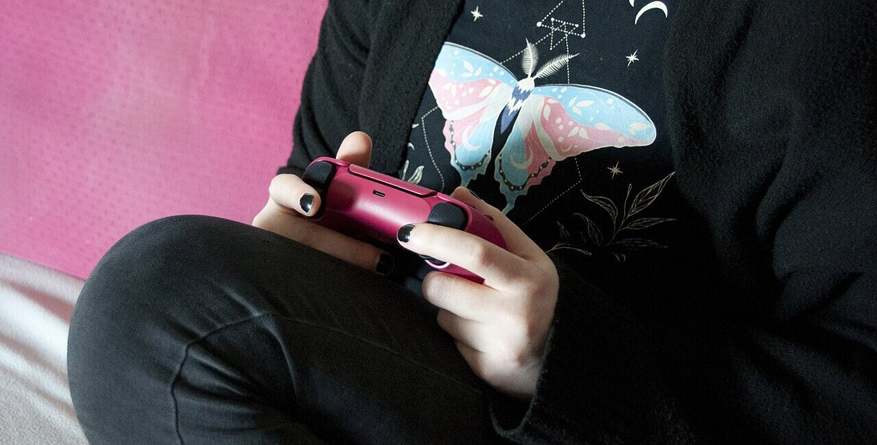 Person holding a pink PlayStation 5 DualSense controller with thumbs resting on its analog sticks