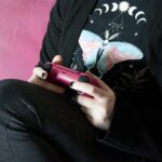 Person holding a pink PlayStation 5 DualSense controller with thumbs resting on its analog sticks