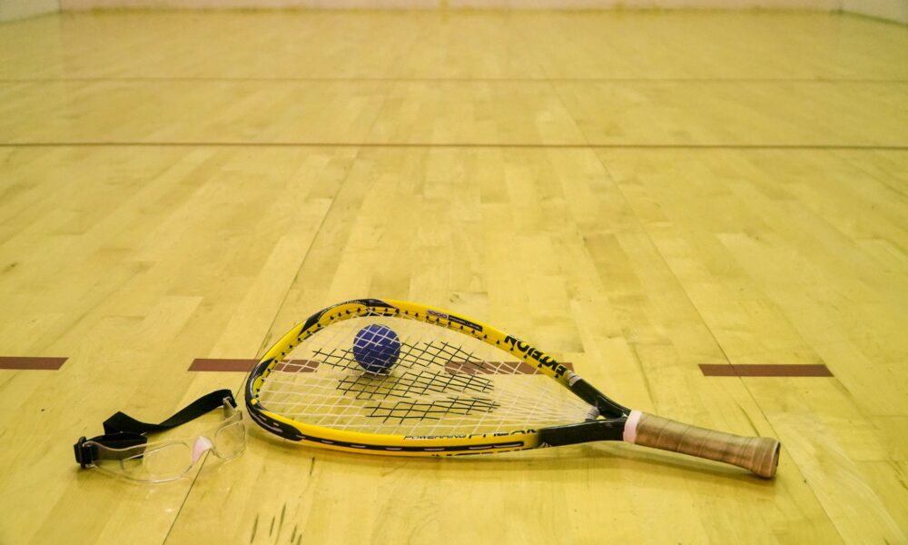Real racquetball racquet with black ball and safety goggles on the wooden floor of a racquetball court