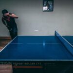 Real indoor table tennis player striking a ping pong ball over the net during a rally