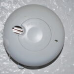 Photograph of a real ceiling-mounted smoke alarm with central test button