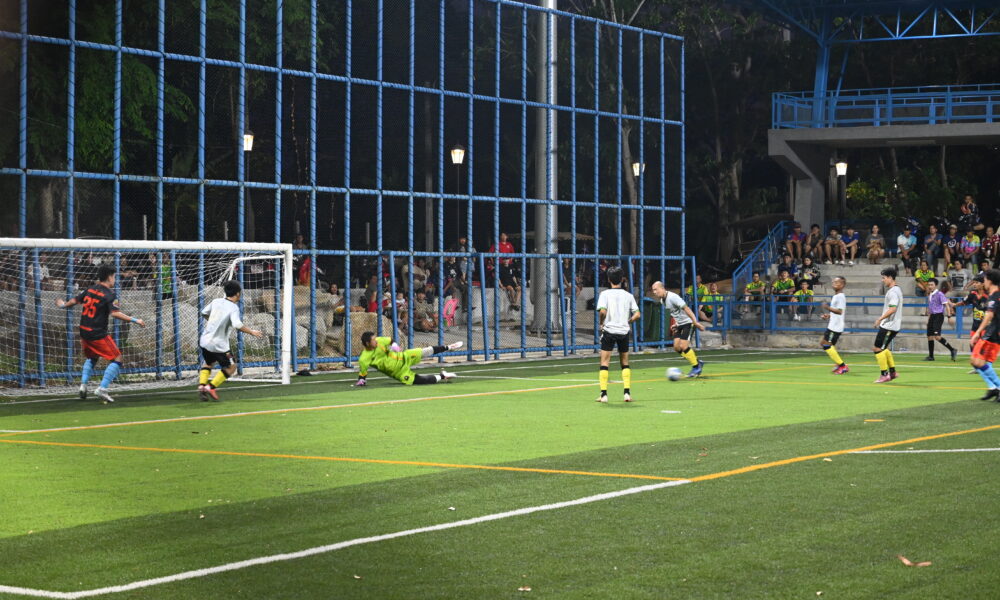 Soccer players attacking the penalty area as a goalkeeper prepares to stop a shot in a night match