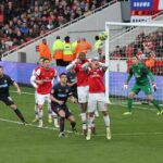 Arsenal defenders and opposing attackers gather in the penalty area to defend a corner kick