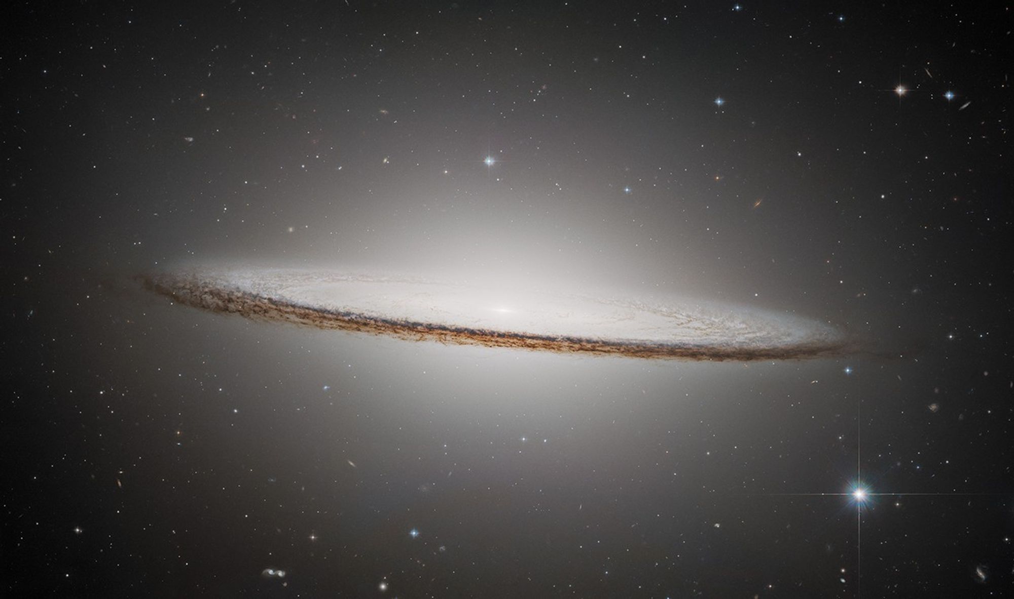 Real ESA NASA Hubble 2025 photograph of Sombrero Galaxy M104 showing a broad central luminous bulge cut across by an edge-on dark dust ring