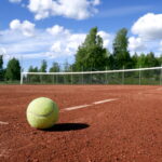 Yellow tennis ball resting on outdoor tennis court surface near court lines
