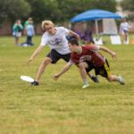 Two ultimate frisbee players dive toward a flying disc during a game