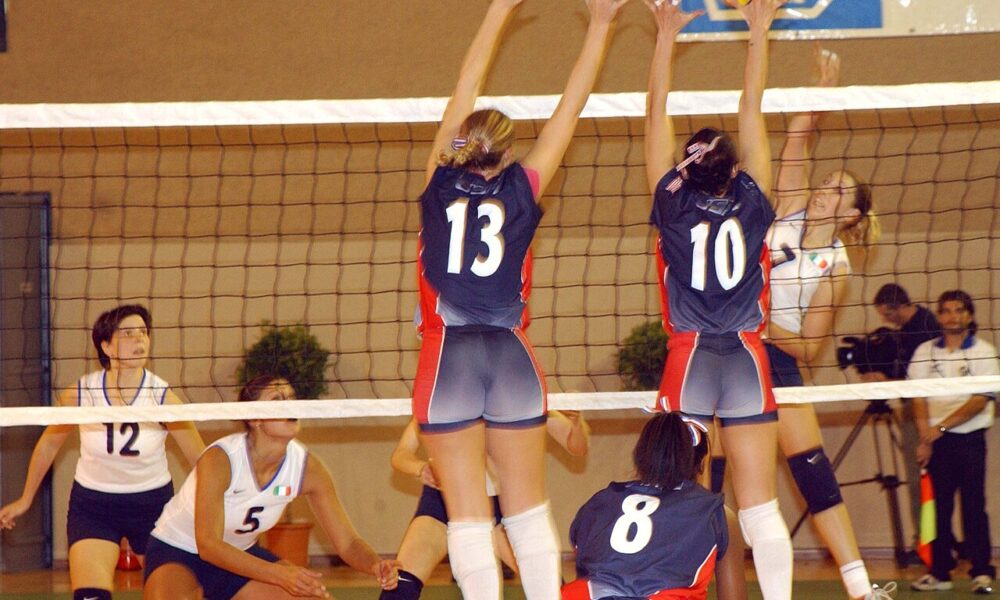 Real indoor volleyball match with two athletes blocking an attack across a regulation net