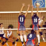 Real indoor volleyball match with two athletes blocking an attack across a regulation net