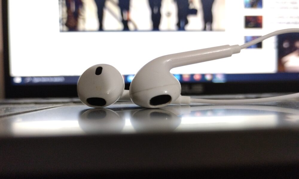 Pair of wired earphones placed on a laptop in front of a computer screen