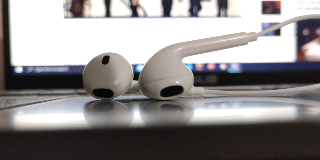 Pair of wired earphones placed on a laptop in front of a computer screen