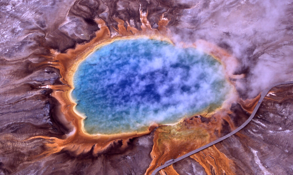 Real aerial photo of Grand Prismatic Spring in Yellowstone with vivid blue central pool orange microbial mats steam and boardwalk
