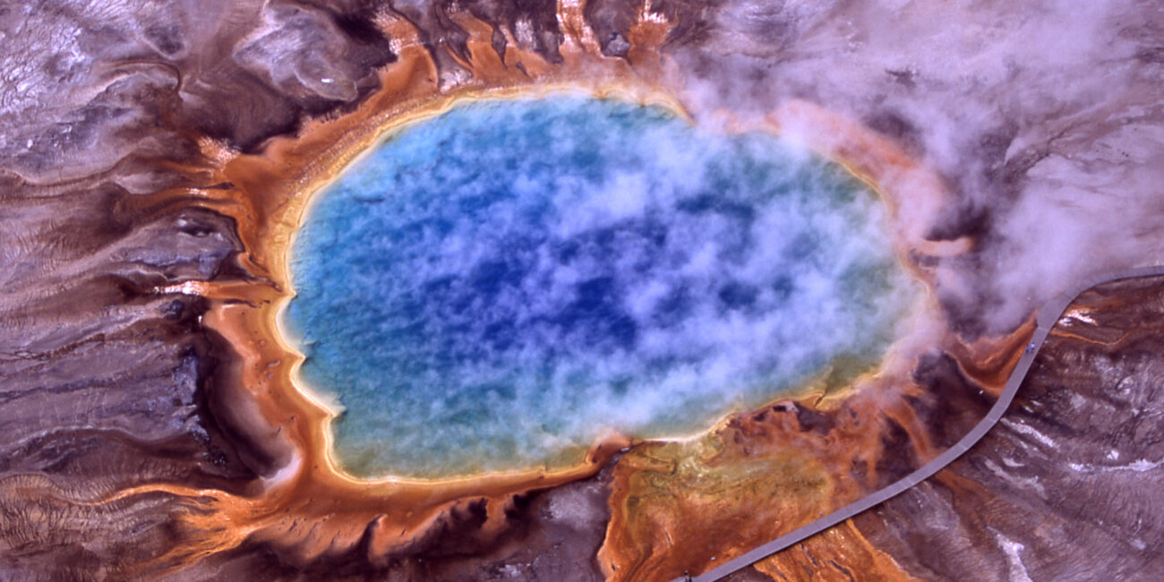 Real aerial photo of Grand Prismatic Spring in Yellowstone with vivid blue central pool orange microbial mats steam and boardwalk