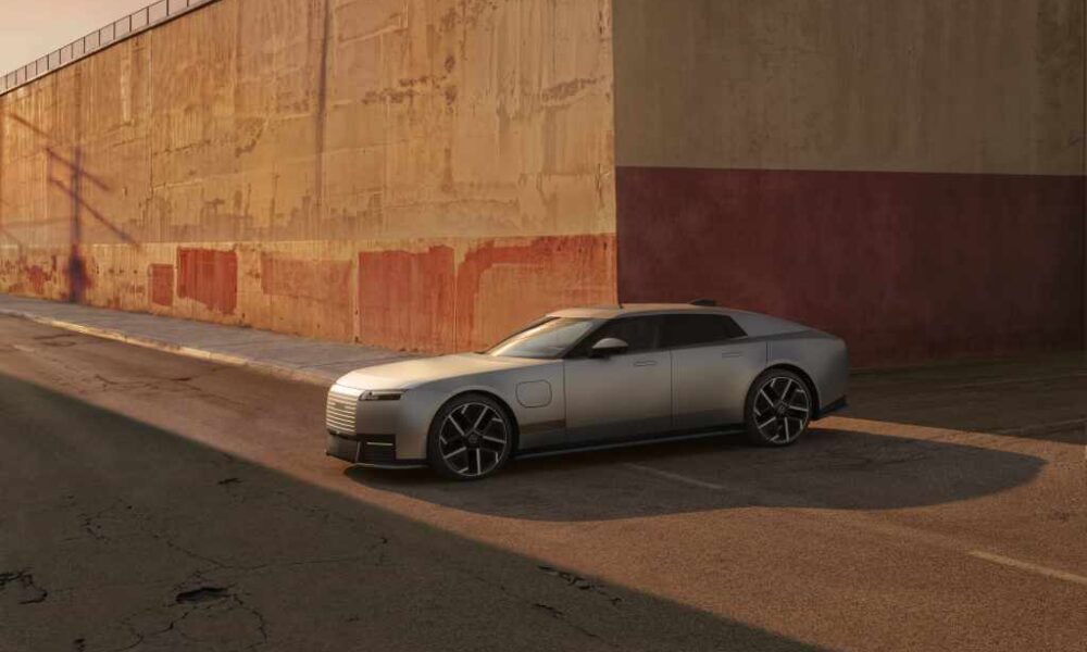 Silver Jaguar Type 01 electric grand tourer parked beside an industrial wall at sunset.