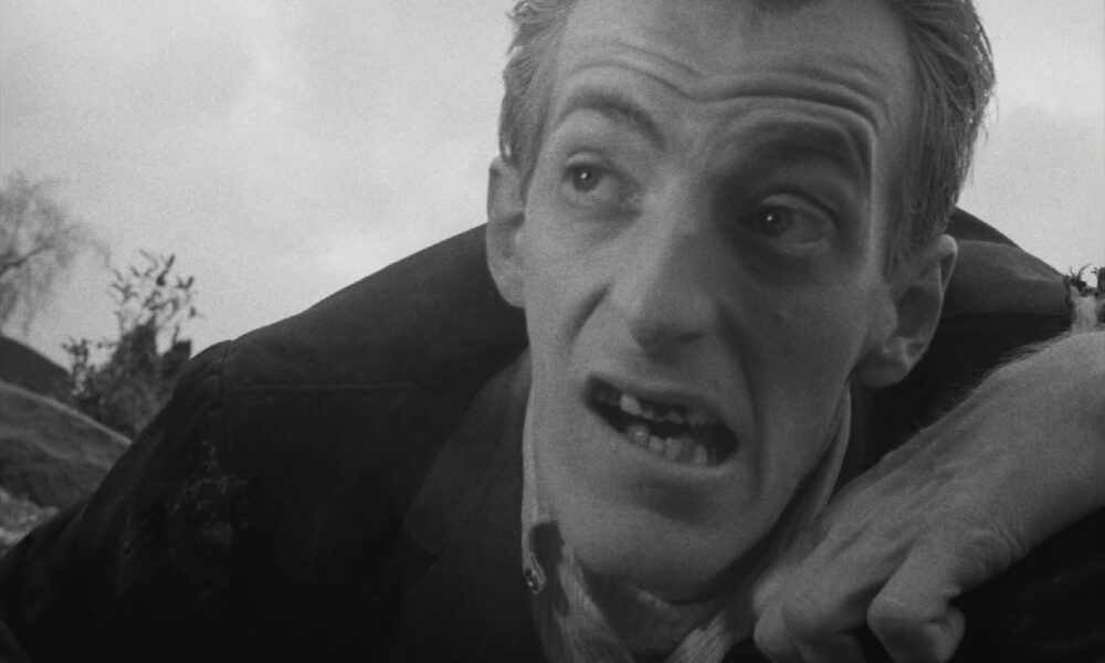 Actual black-and-white frame from George A. Romero's Night of the Living Dead (1968), showing Bill Hinzman as the cemetery ghoul
