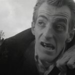 Actual black-and-white frame from George A. Romero's Night of the Living Dead (1968), showing Bill Hinzman as the cemetery ghoul
