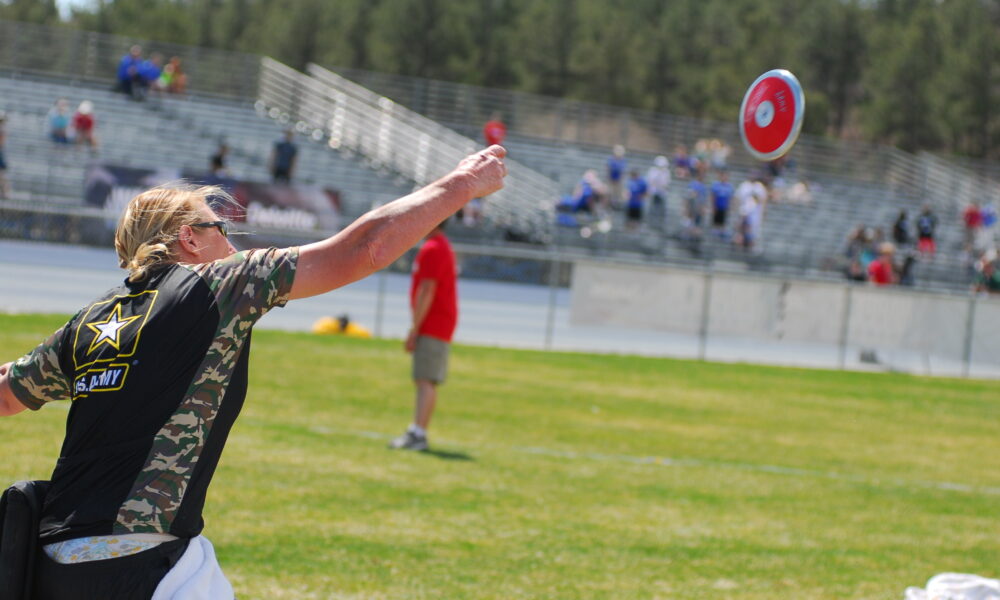Real U.S. Army photograph of veteran Chanda Gaeth throwing a discus from a seated position during the 2013 Warrior Games